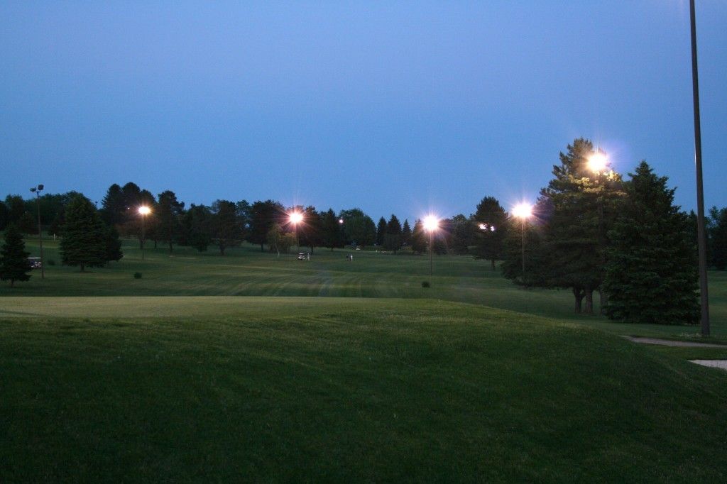 A golf course is lit up at night with a blue sky in the background