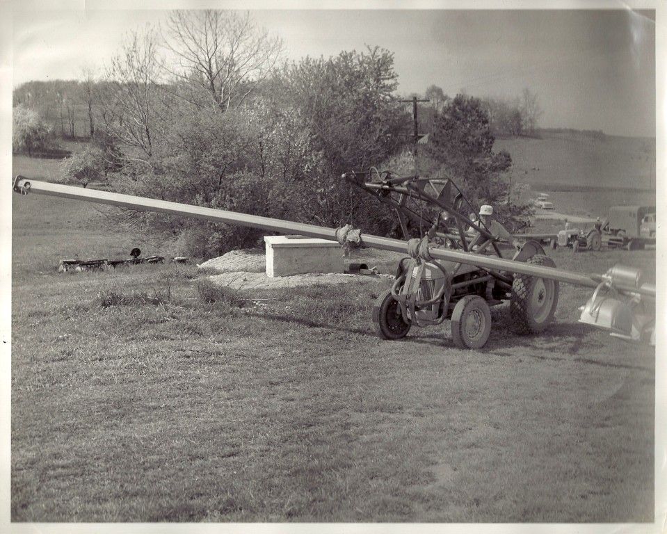 A black and white photo of a tractor pulling a large pipe