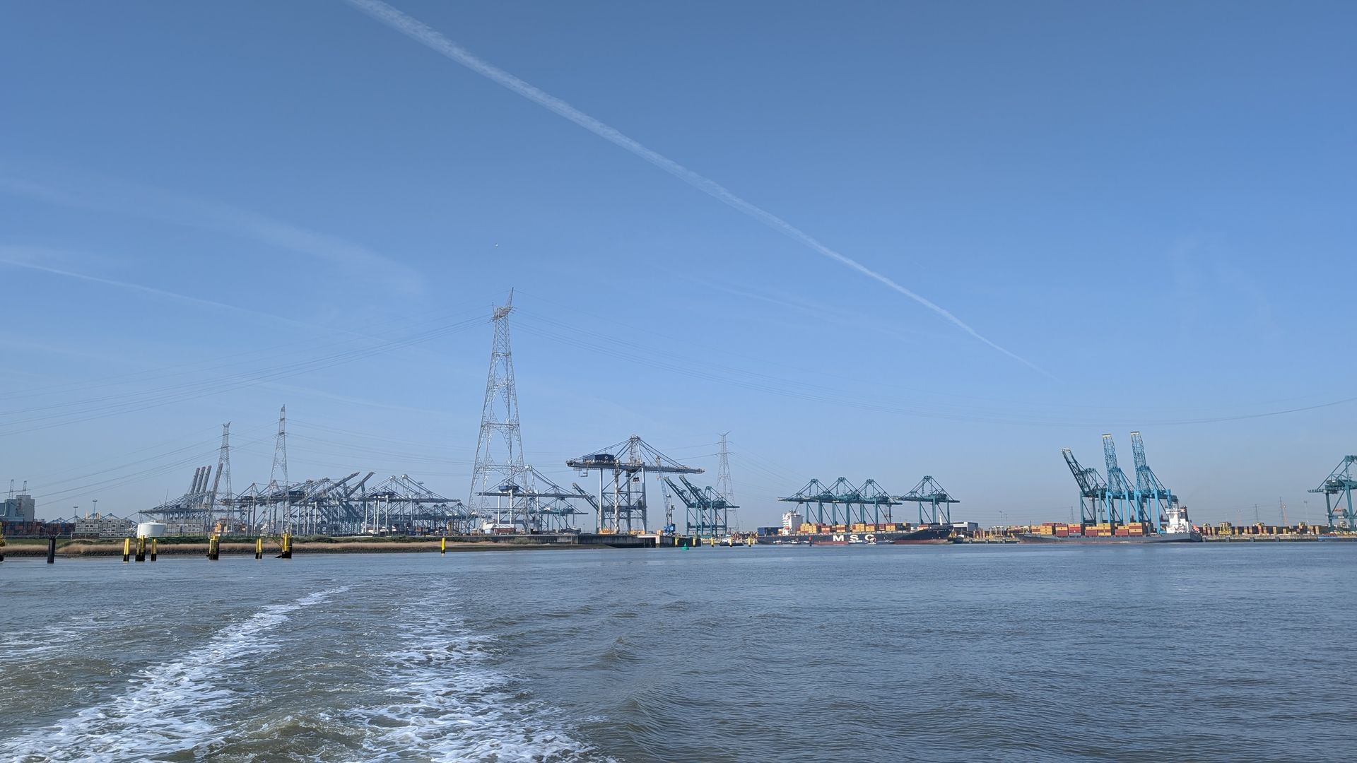 Container cranes and a cargo ship at a busy port across calm blue water under a clear sky