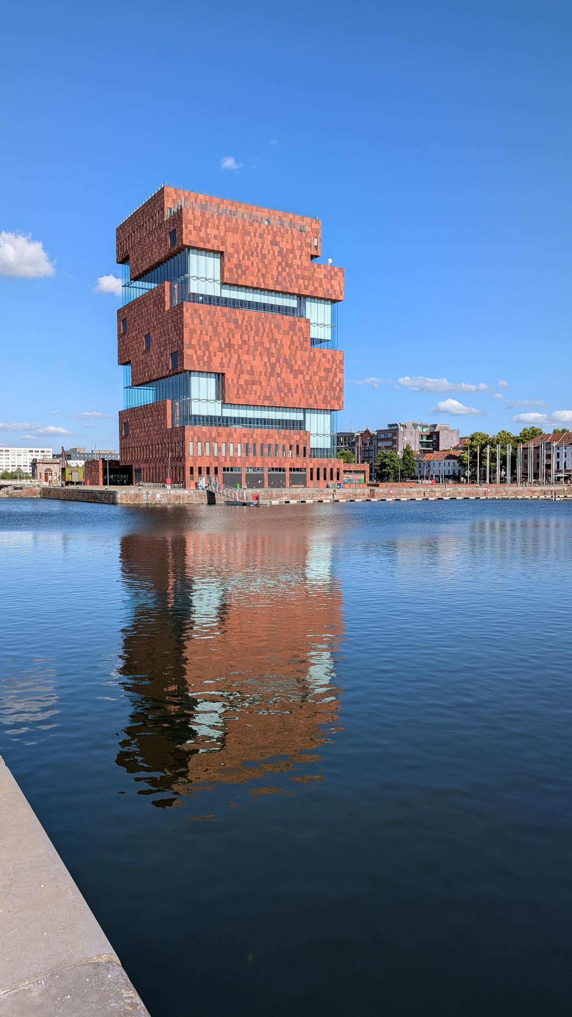 MAS Museum in Antwerp, Belgium, brick facade, reflective windows, water, blue sky.