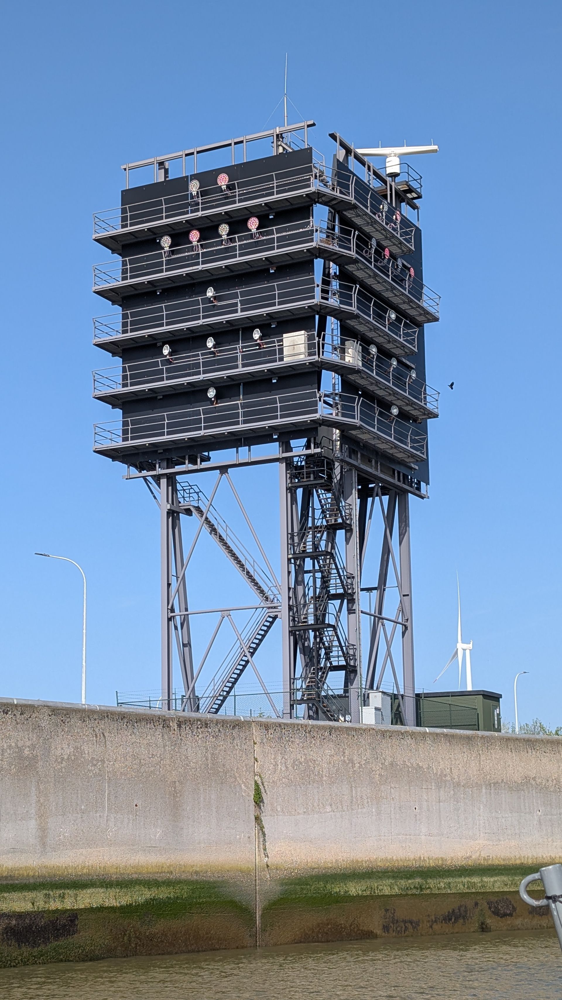 Tall metal radar tower on a concrete base against a clear blue sky