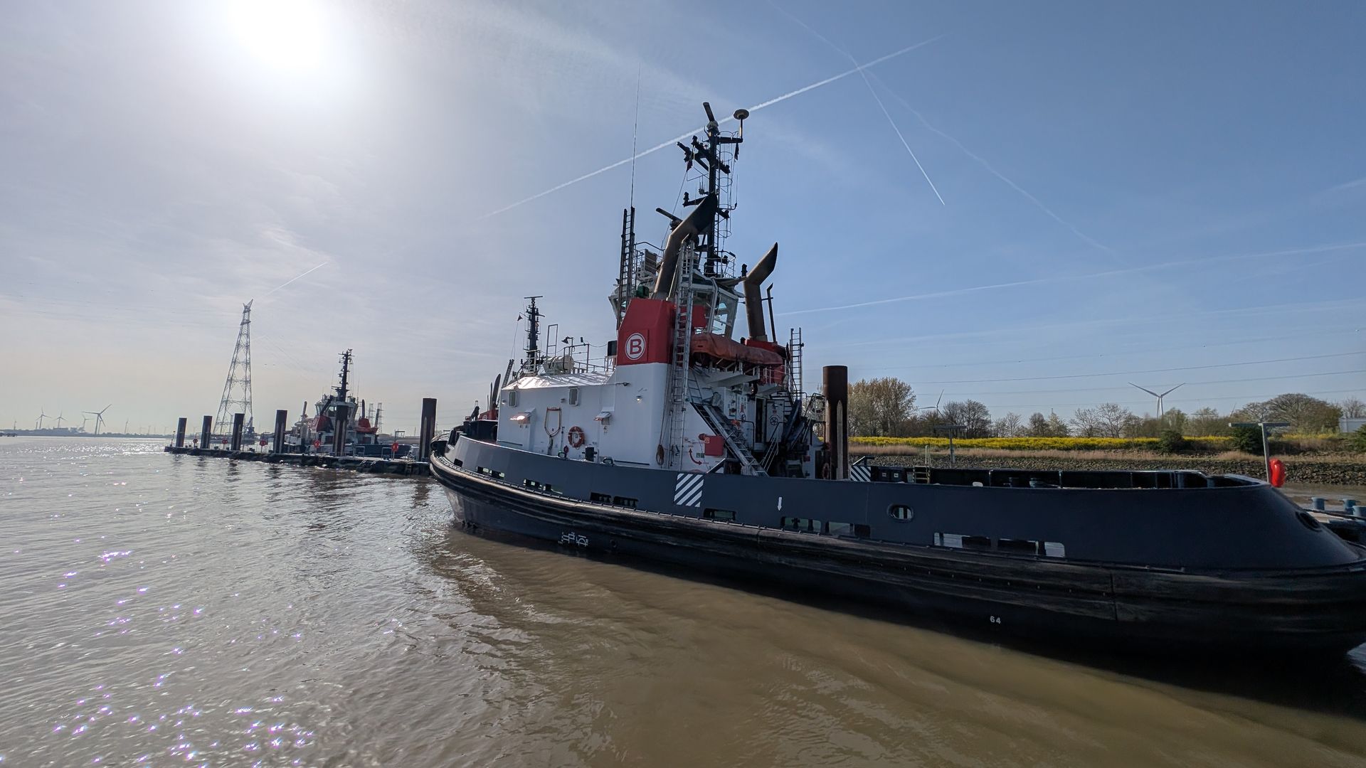Tugboat and workboats lined along a muddy riverbank under a bright sky