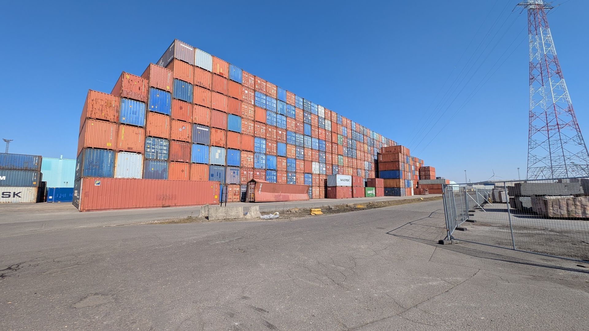 Shipping containers stacked high at a port under a clear blue sky.