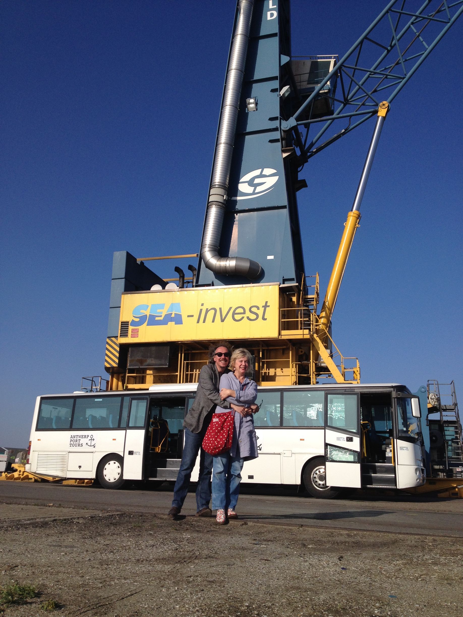 Couple hugging in front of a white bus and large blue crane with 
