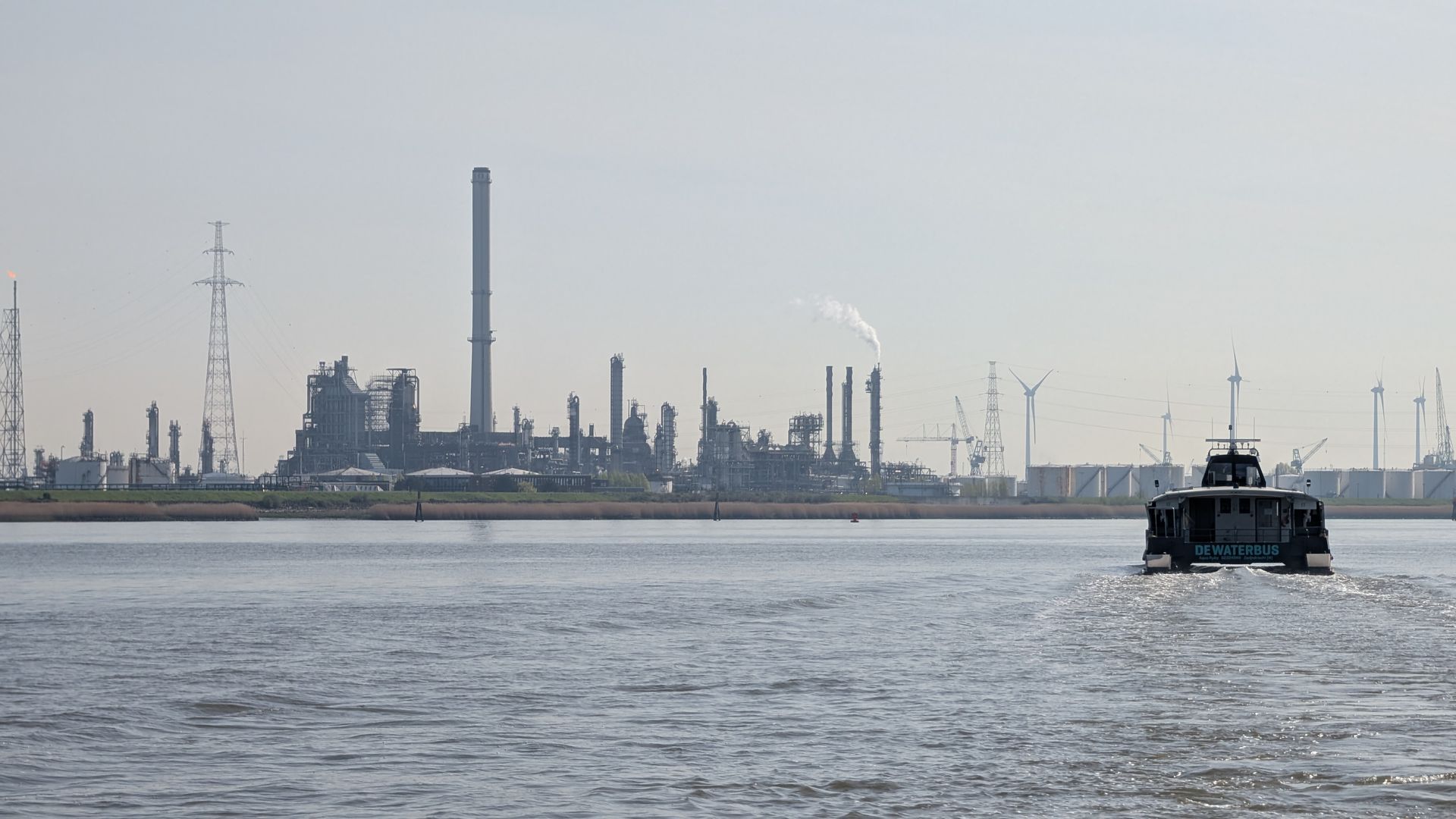 Industrial waterfront with smokestacks and a small boat on calm gray water.