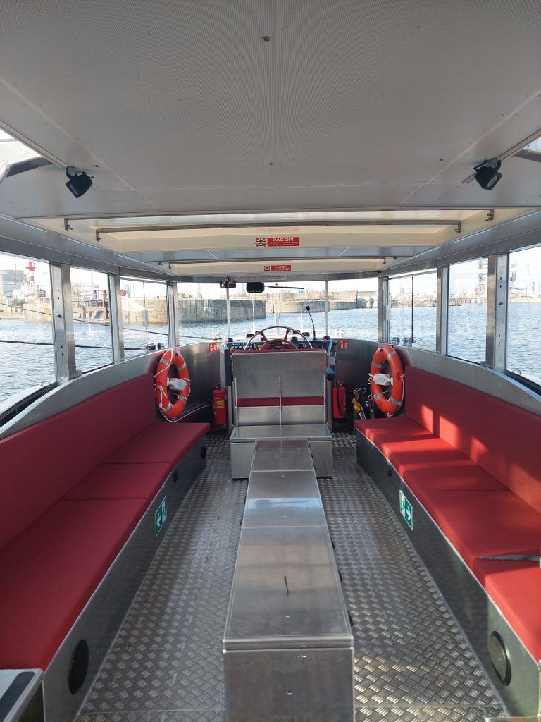 Empty ferry cabin with red benches, metal floor, and life rings by the windows