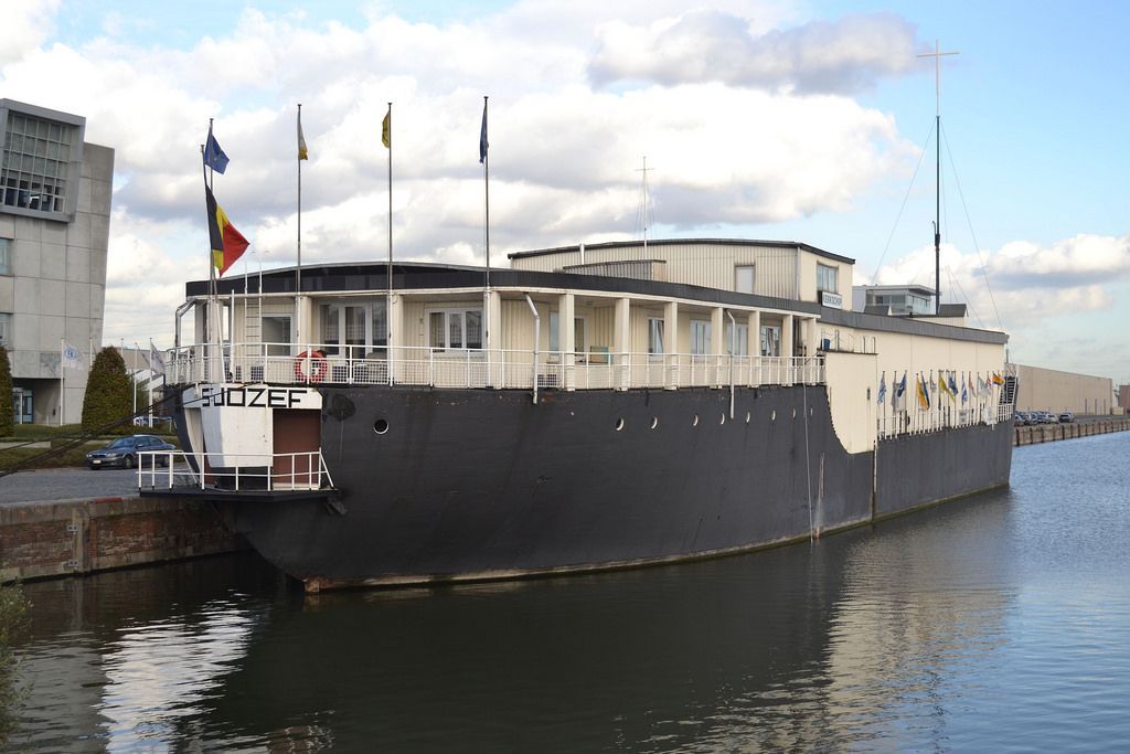 Large black-and-white ship docked on a calm canal beside buildings under a cloudy sky