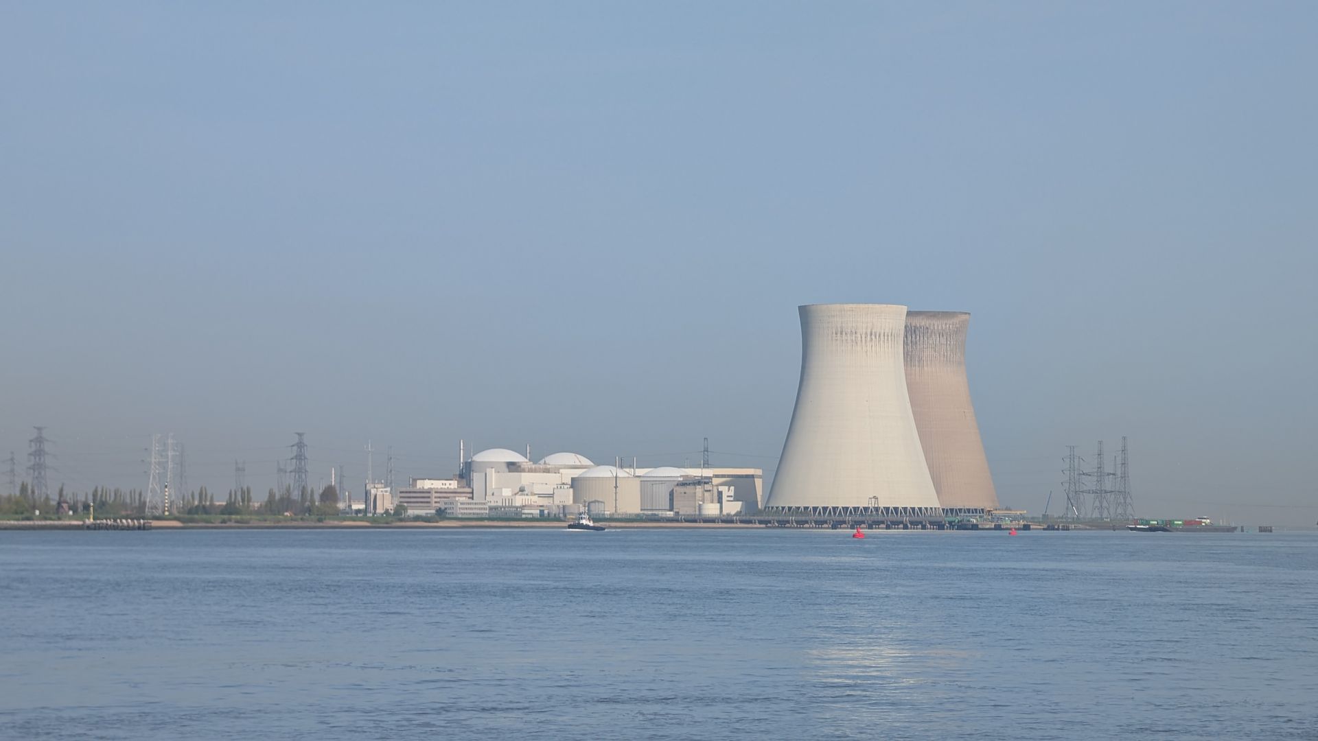 Coastal power plant with a large cooling tower across calm blue water under a clear sky
