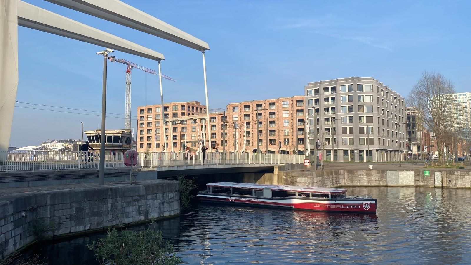 Canal with a moored boat, bridge, and modern apartment buildings on a sunny day