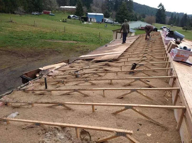Workers repairing a long damaged walkway beside a grassy field and rural buildings