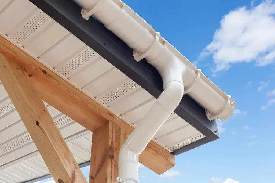 White gutter and downspout on a wooden roof eave against a blue sky