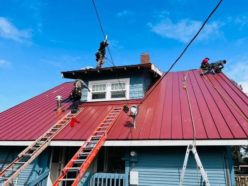 Workers repairing a red metal roof with ladders on a house