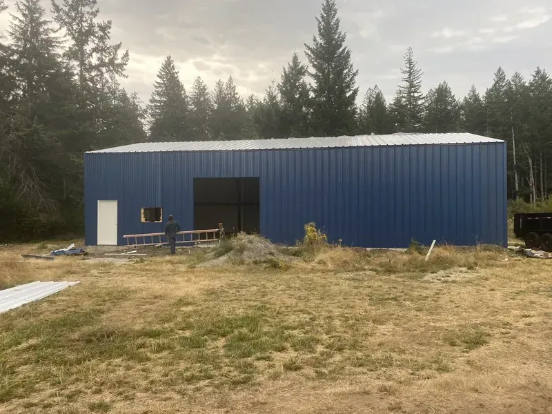 Blue metal building in a grassy clearing surrounded by trees under an overcast sky