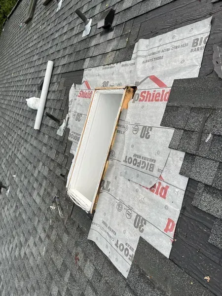Roof shingles with a partially covered skylight opening and white vent pipe