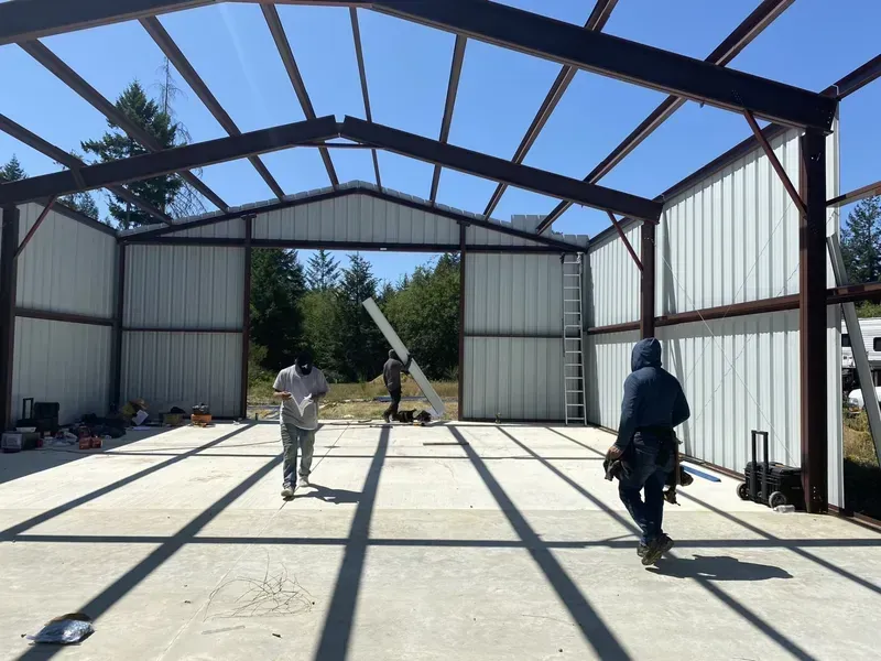 Workers inside a steel-frame building under construction with a crane lift and concrete floor.