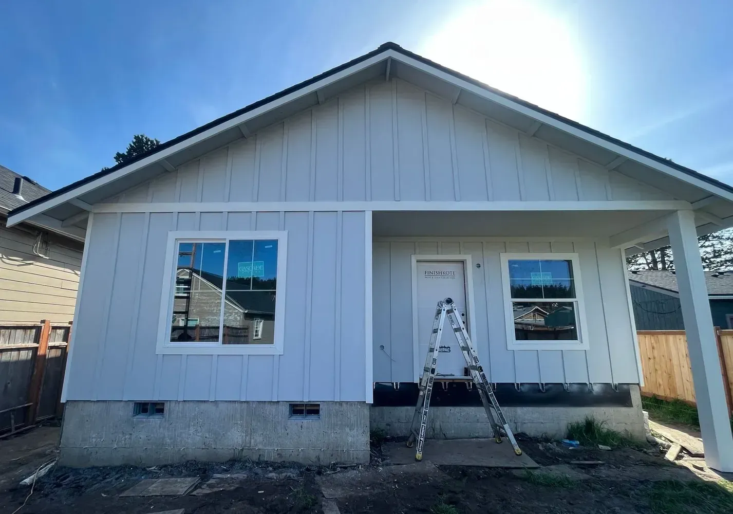 Front view of a white house under construction with a ladder on the porch and bright sun overhead