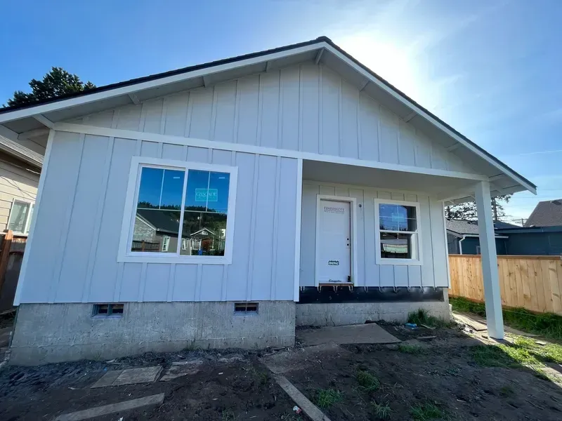 Small white single-story house exterior with porch, gray roof, and front windows.
