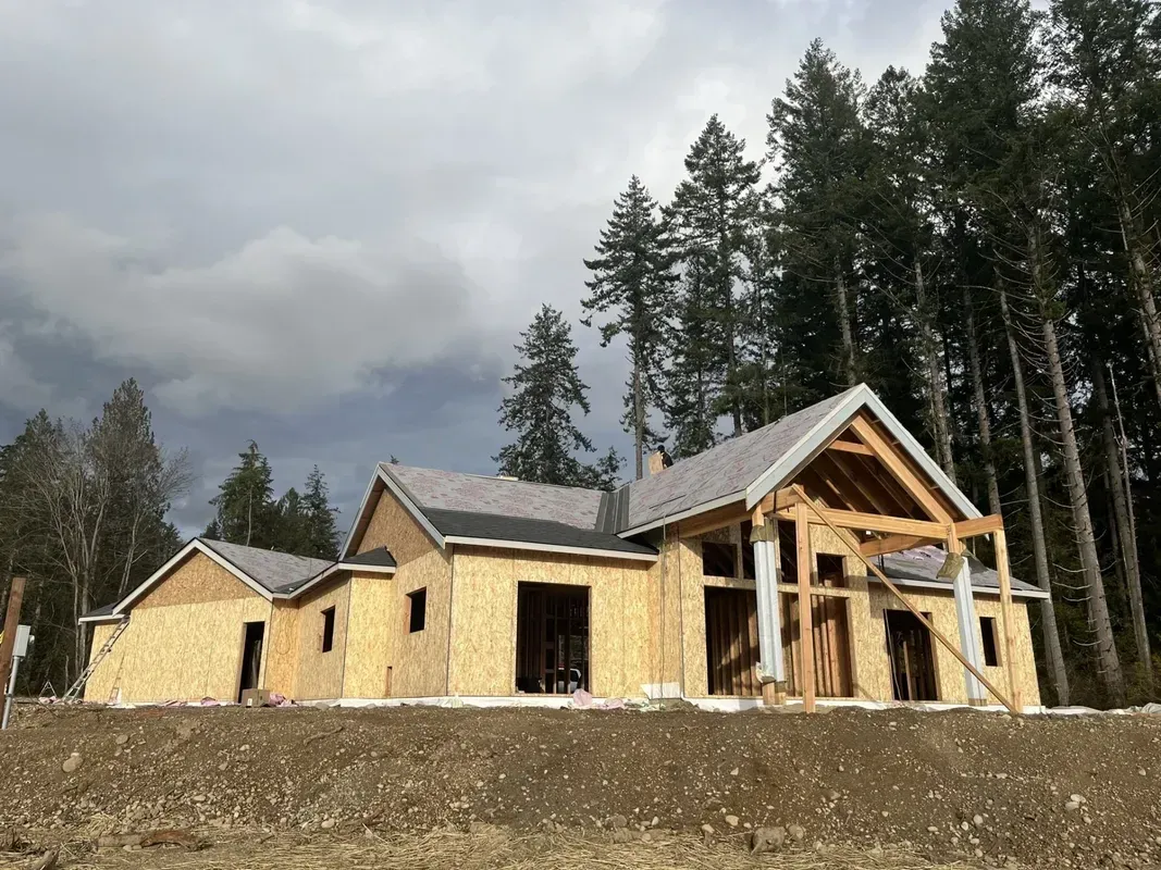 Partially built wooden house under construction on a dirt lot beneath a cloudy sky