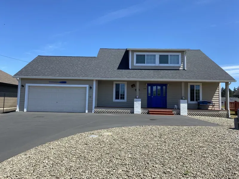 Suburban house with gray roof, blue front door, garage, and gravel driveway under a clear sky