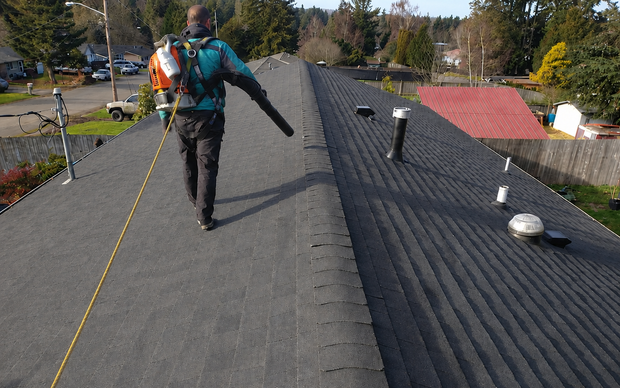 Contractor blowing debris from residential asphalt shingle roof