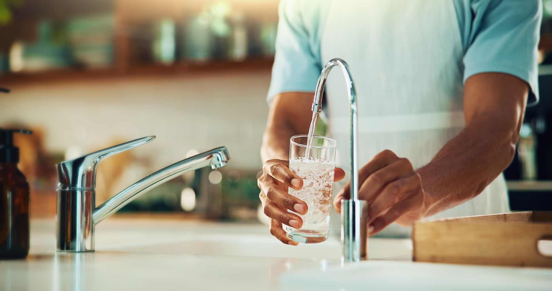Water treatment: a person filling a glass of water from a kitchen faucet.]