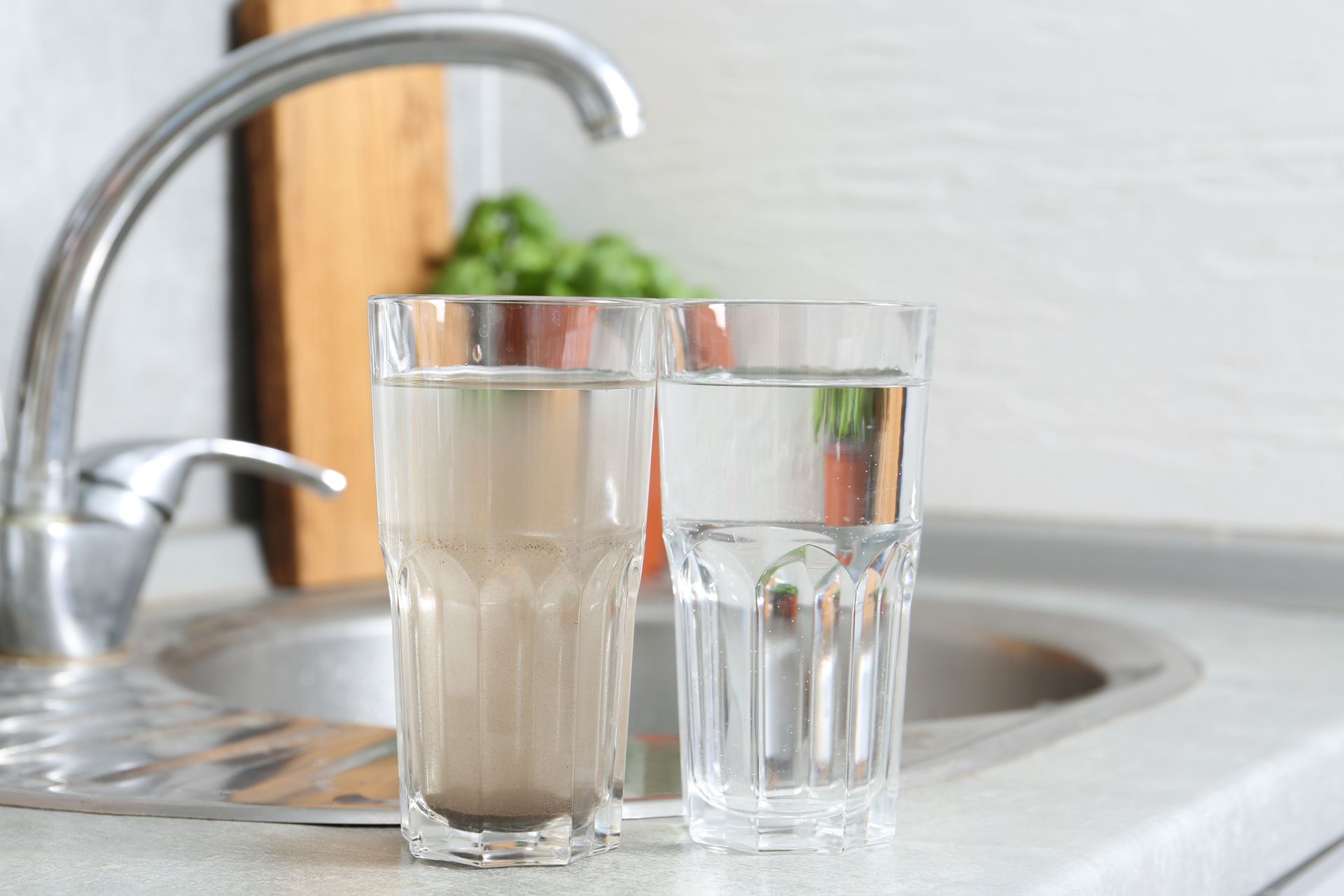 Two glasses comparing clean and dirty tap water by a sink
