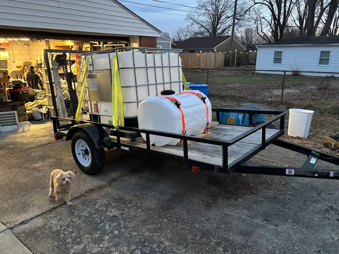 A dog is standing next to a trailer with a tank on it.