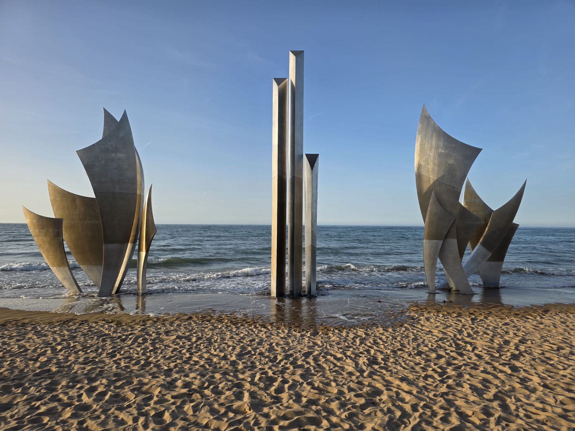 Sculpturale metalen zeilen op een zandstrand met de oceaan en de blauwe lucht op de achtergrond.