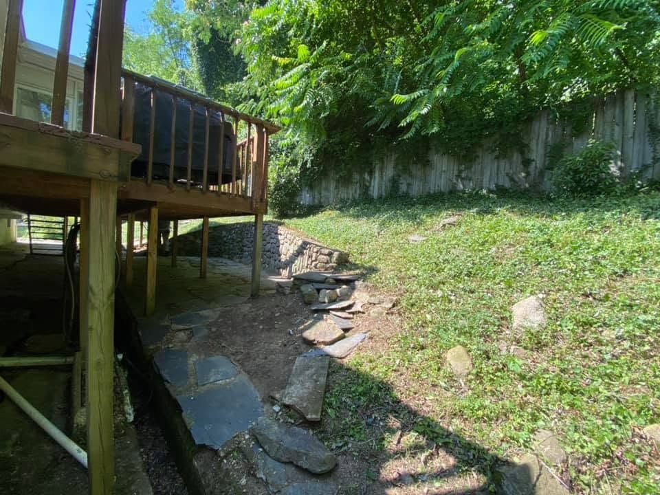 Backyard deck beside a dry, grassy slope with scattered rocks and a shaded drainage ditch