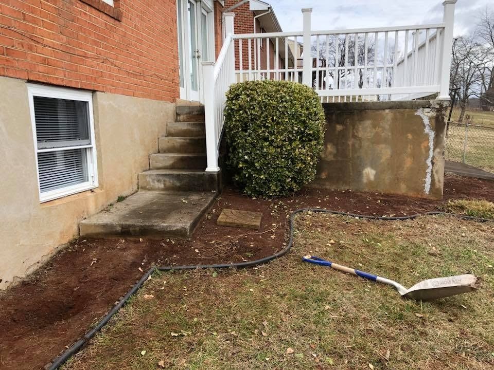 Backyard patio with steps, a large bush, and a shovel on the ground near a brick house