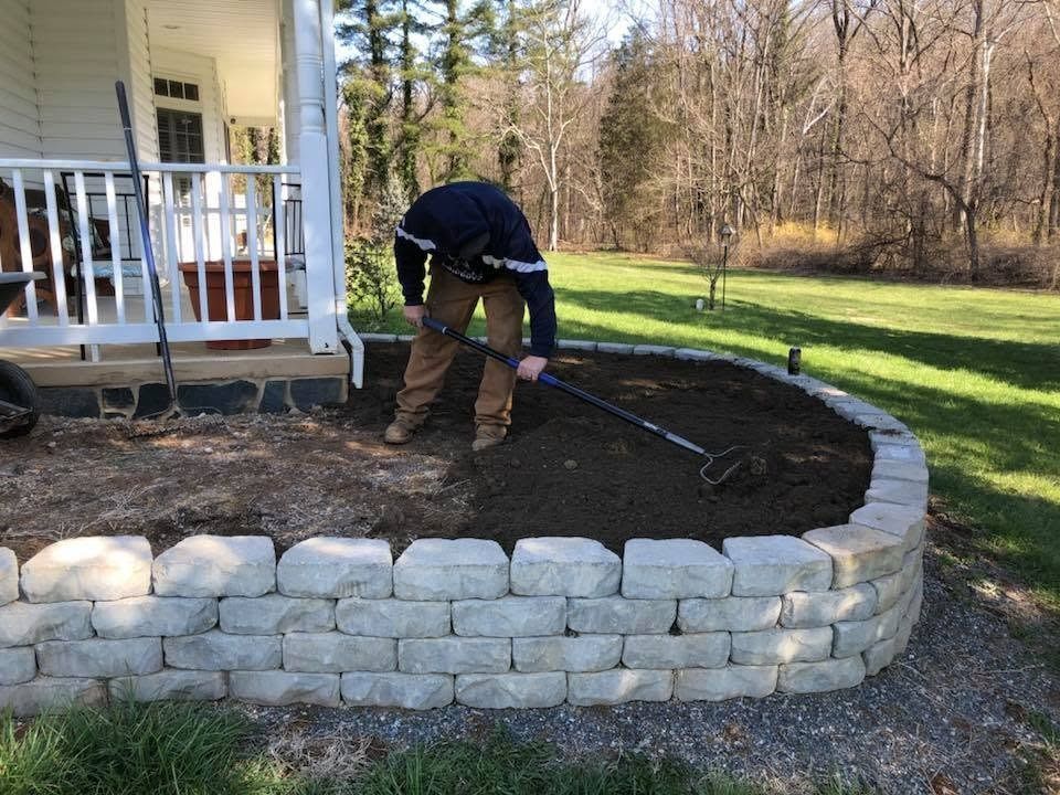 Person raking soil beside a house porch and newly built stone retaining wall