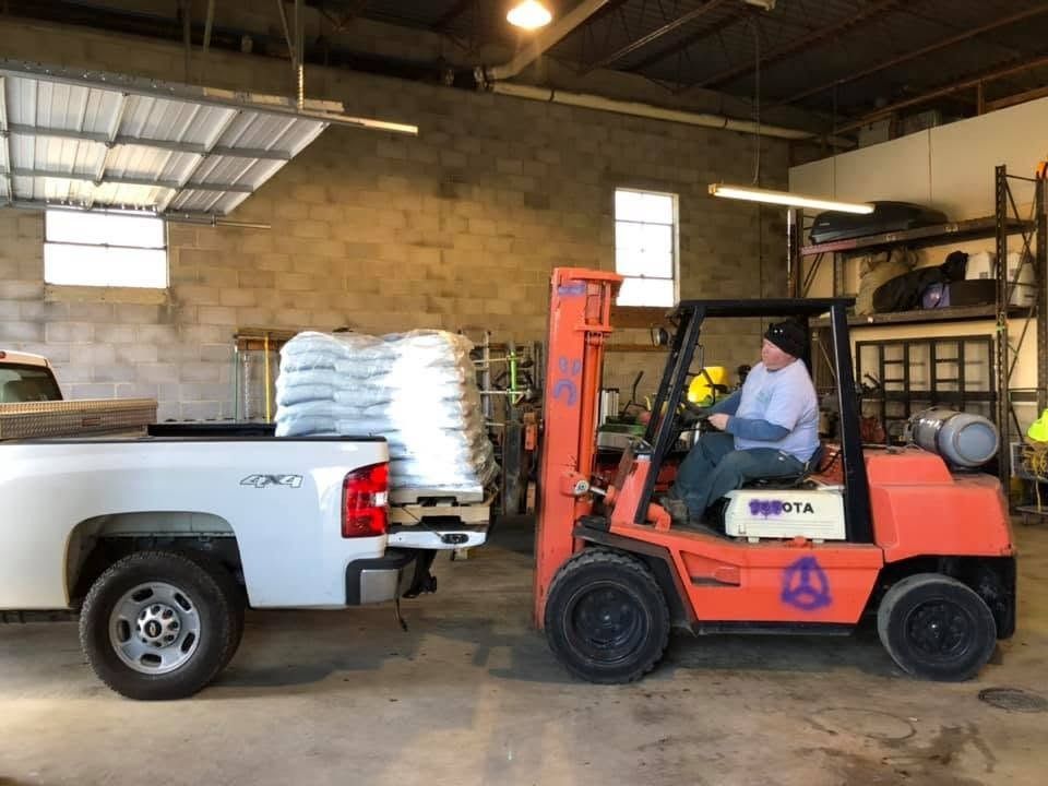 Orange forklift beside white pickup truck inside a warehouse, with a worker seated in the forklift.