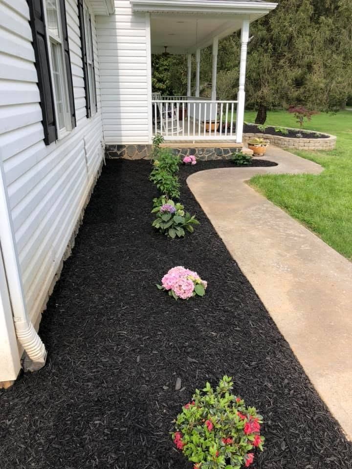 Front porch walkway with black mulch and pink flowers beside a white house