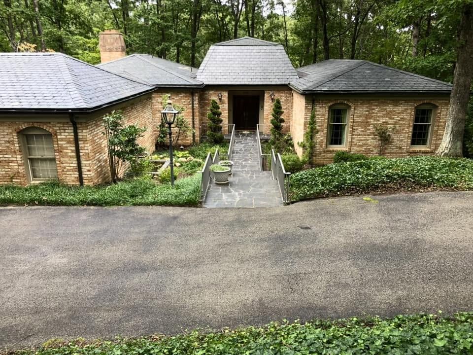 Brick house with dark gray roofs, central walkway, and wooded landscaping