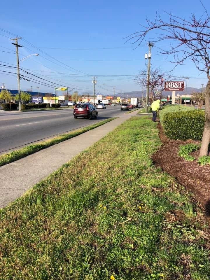Roadside sidewalk beside a busy street, with a worker in a yellow vest near an H&R Block sign.