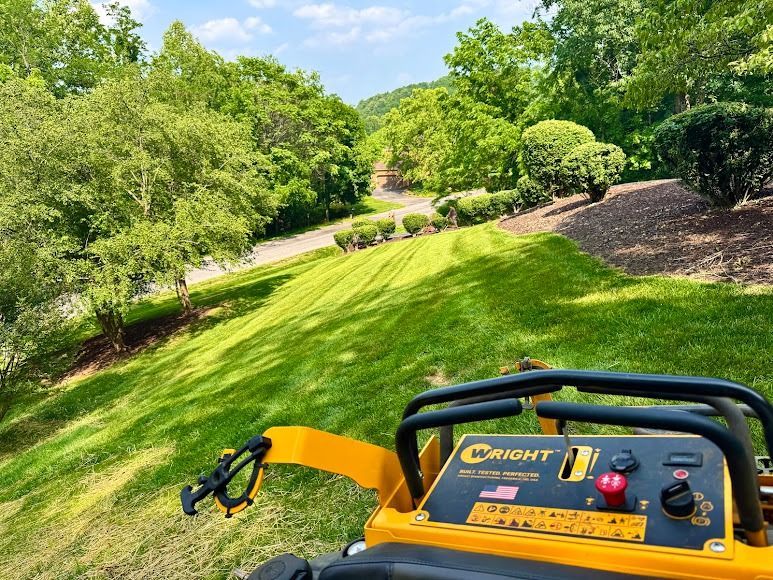 Yellow lawn mower on a sunny green hillside with trees and a curving path