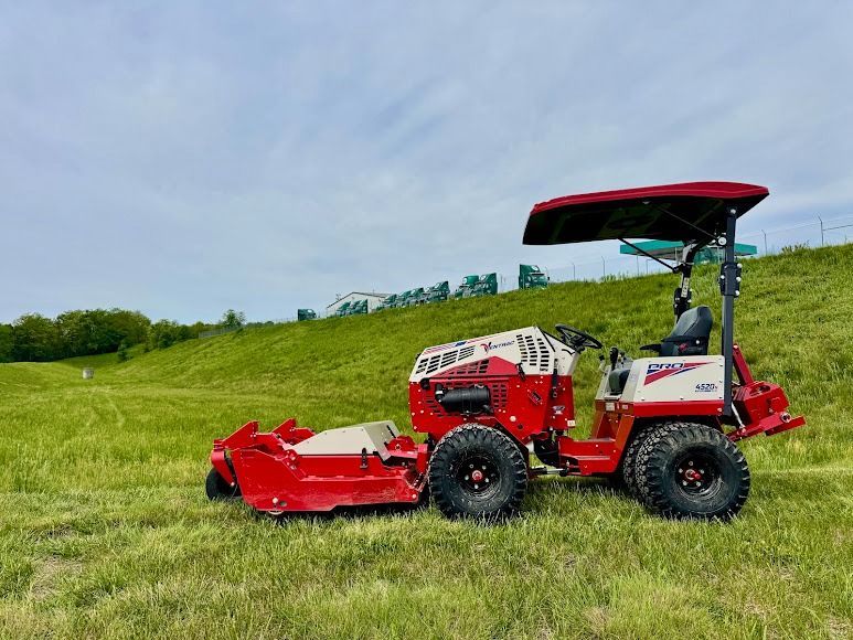 Red riding lawn mower on a grassy hillside under a cloudy sky