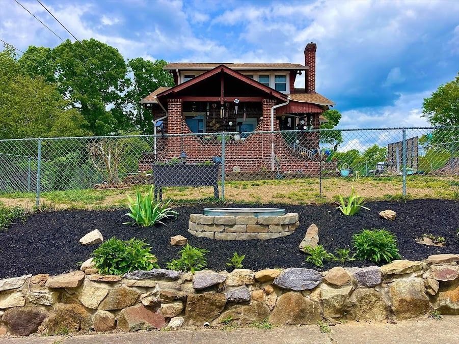 Stone retaining wall and landscaped garden in front of a red brick house with a fenced yard.