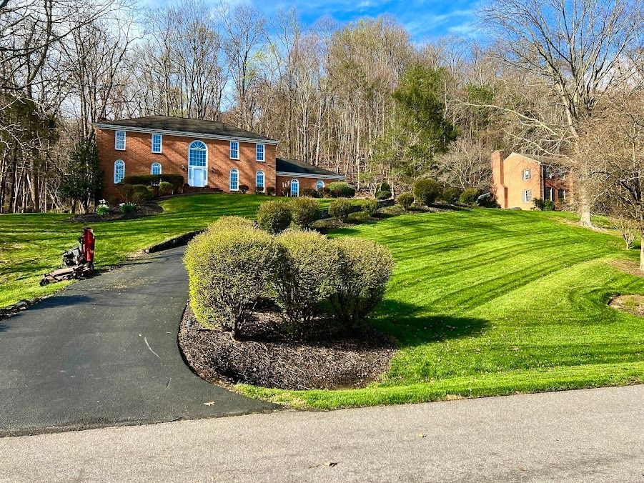 A red-brick house on a grassy hill with a curved driveway and leafless trees under a blue sky.