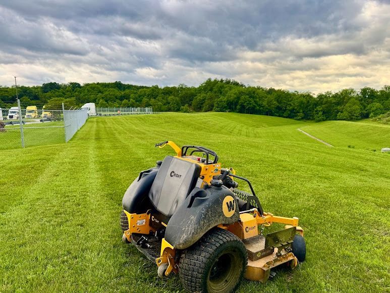 Yellow-and-black riding mower on a green sports field under cloudy skies