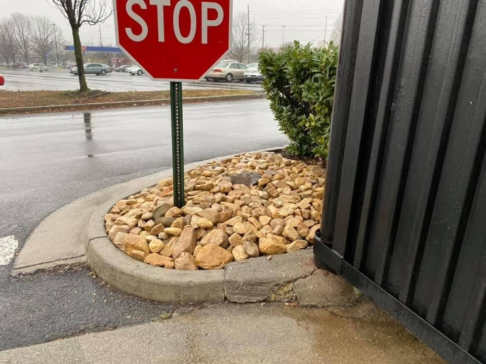 Stop sign beside a rock bed and curb on a rainy roadside corner