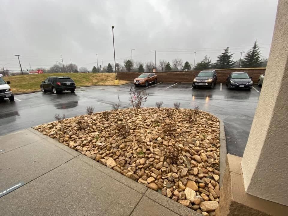 Wet parking lot with parked cars beside a stone landscaping bed on a rainy day
