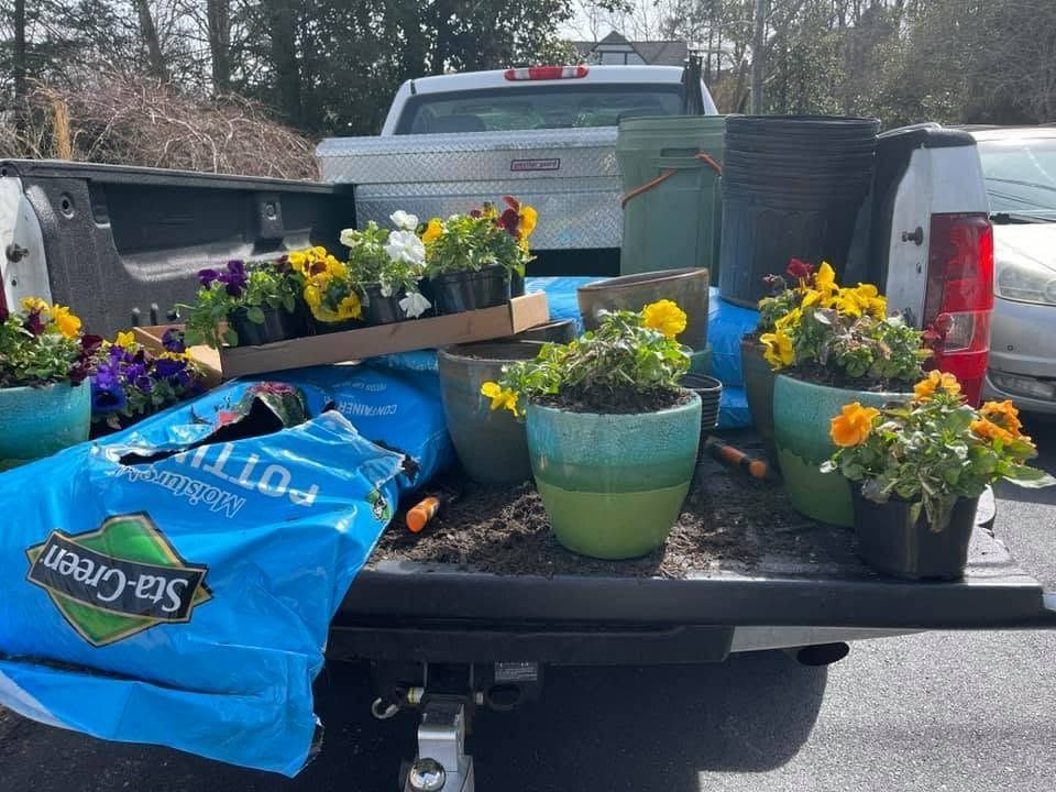 Pickup truck bed filled with colorful potted flowers, plants, and bags of soil