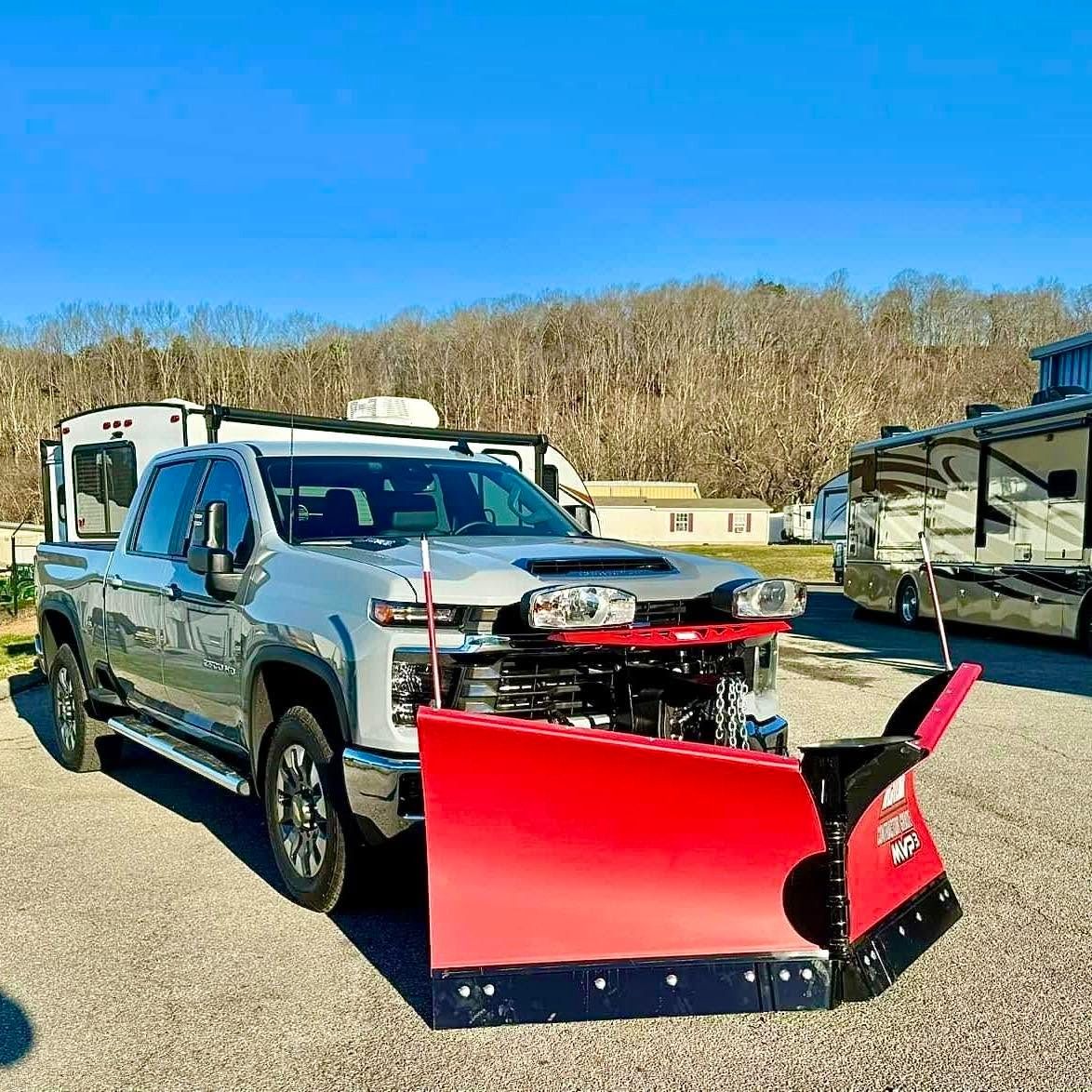 Silver pickup truck with a red snow plow parked outdoors on a sunny day