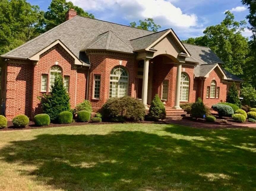 Brick suburban house with a gray roof, arched windows, and a manicured lawn in bright sunlight