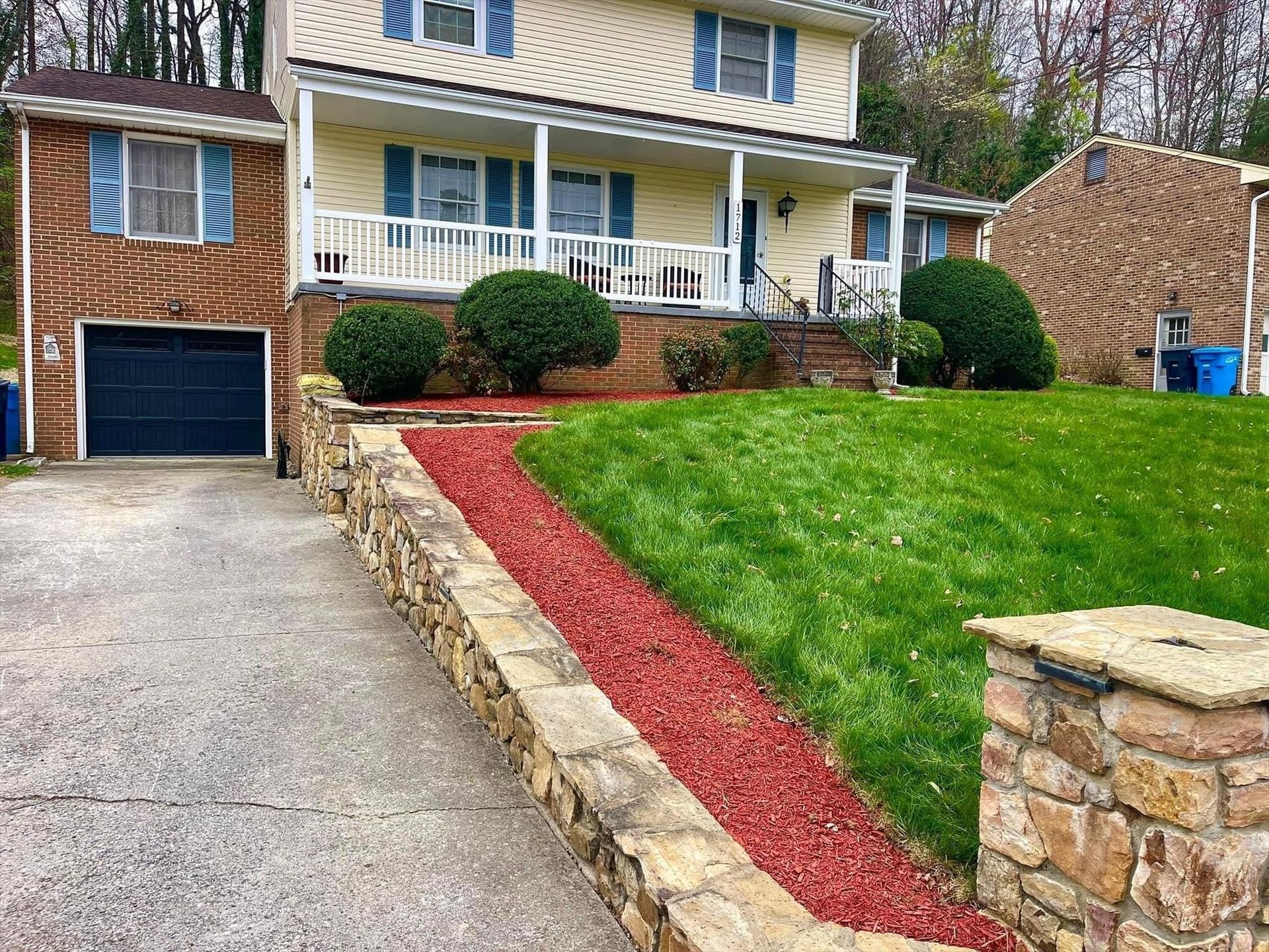 Suburban house with stone walkway, red mulch border, green lawn, and attached garage