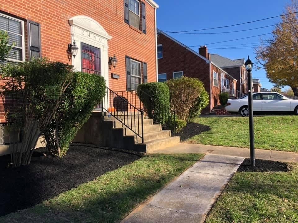 Brick apartment row with front steps, trimmed hedges, and a sidewalk on a sunny day