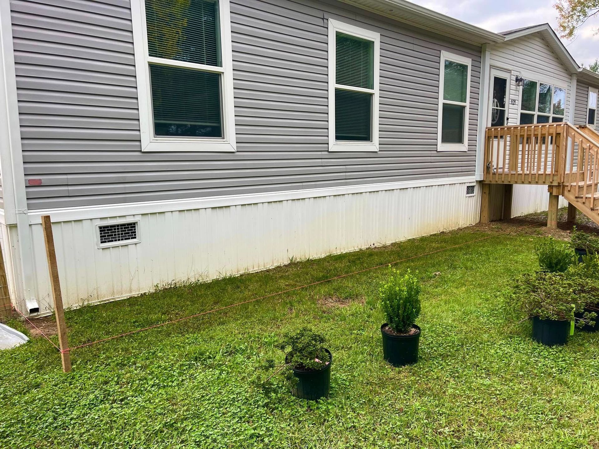 Mobile home exterior with gray siding, white skirting, and potted plants on a grassy lawn