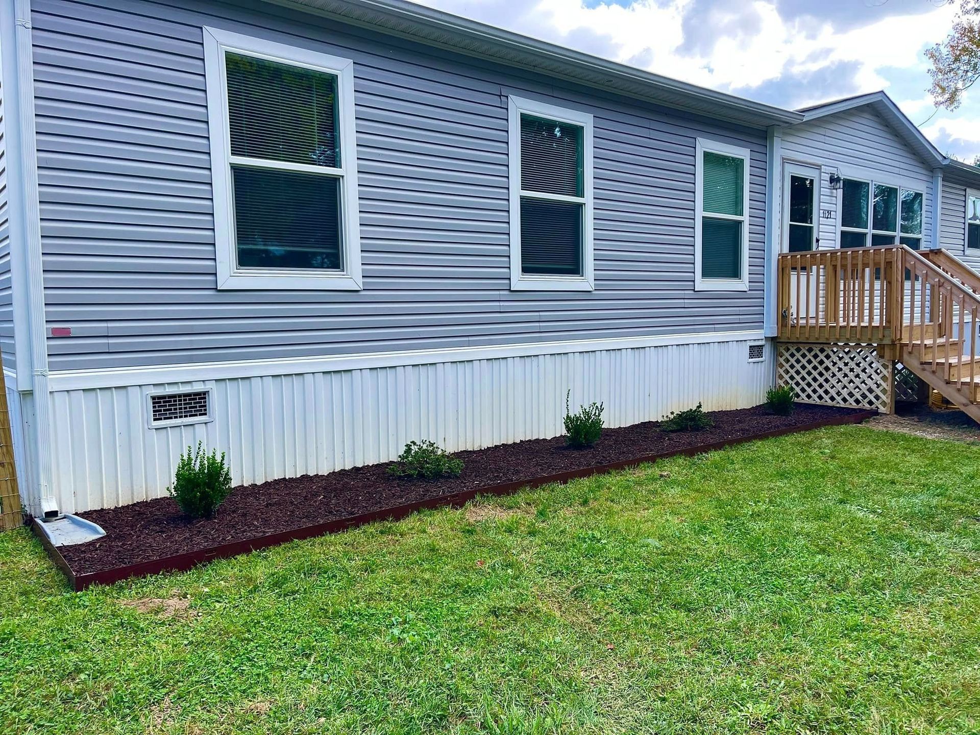 Exterior of a gray mobile home with white trim, small porch, windows, and a grassy yard