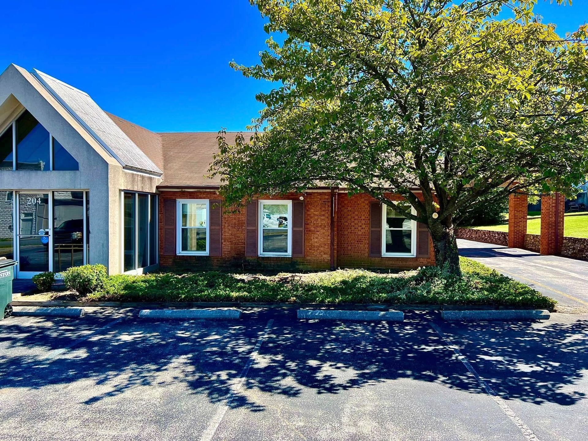 Brick office building with large windows and a leafy tree casting shadows on the sidewalk